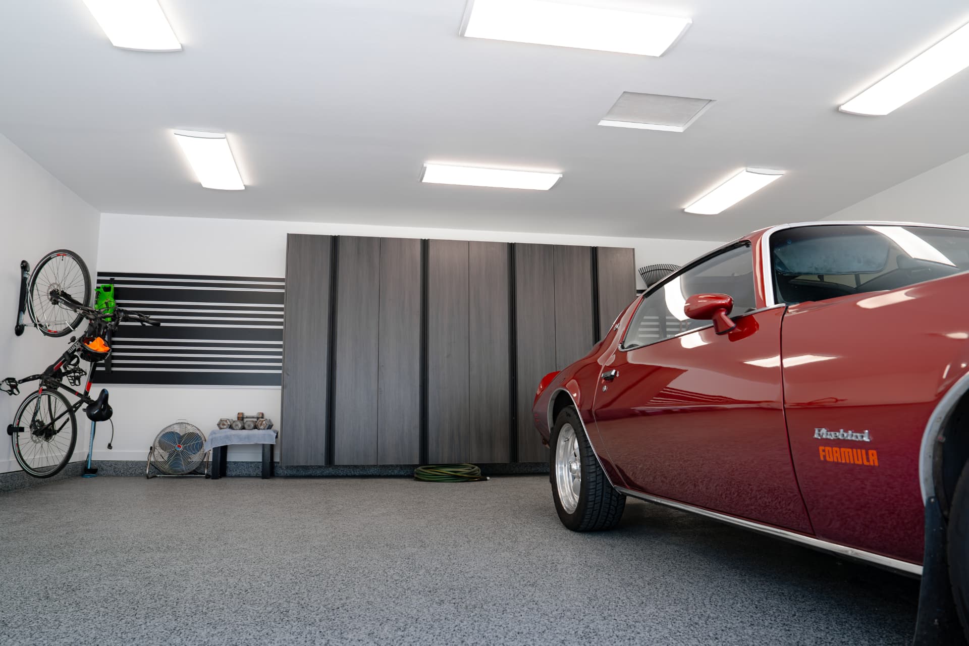 Finished garage with a coated flake floor, slatwall storage and a classic Firebird parked inside